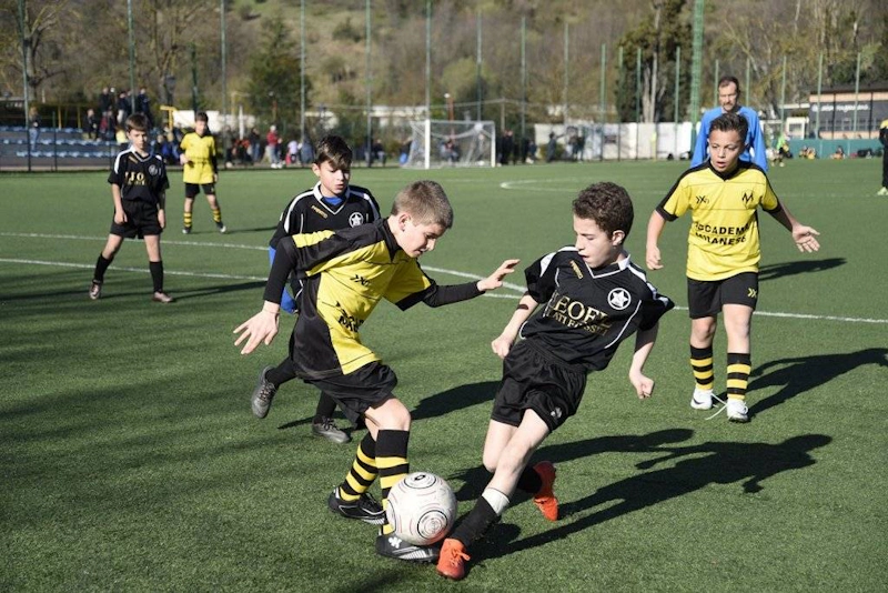 검은색과 노란색 축구 유니폼을 입은 어린이들이 필드에서 축구를 하고 있음