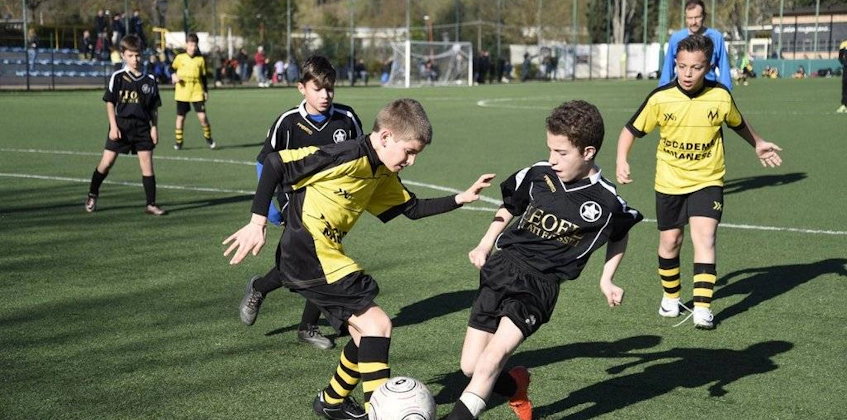Lapset mustissa ja keltaisissa jalkapalloasuissa pelaavat jalkapalloa kentällä