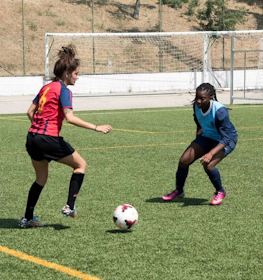 穿着红蓝条纹的女足球员在阳光明媚的日子里对抗穿深蓝色的对手。