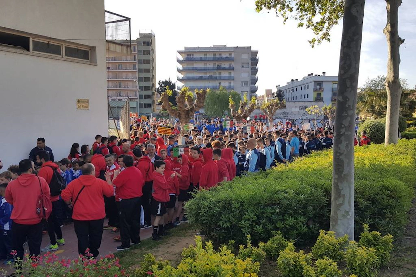 Duże zgromadzenie młodzieżowych drużyn piłkarskich w różnych strojach przygotowujących się do turnieju Trofeo Vila de Lloret w miejskim otoczeniu.