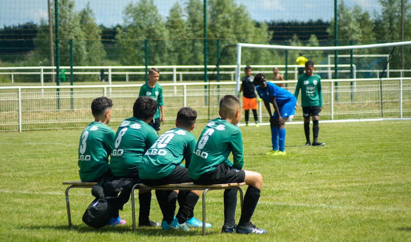 Jugadores de fútbol con camisetas verdes sentados en un banco viendo un partido en la Copa Paris Val d'Europe.