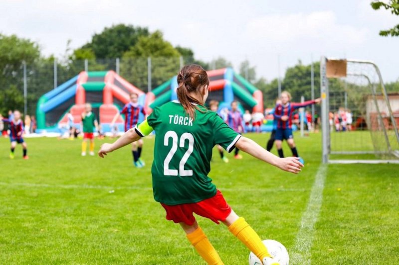 Jogadora de futebol número 22 com camisa verde chutando durante o torneio Laola Cup