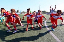 Ενθουσιασμένοι νεαροί ποδοσφαιριστές με κόκκινες και μπλε στολές πανηγυρίζουν στο τουρνουά MICFootball 7