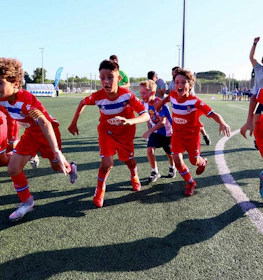 Opgewonden jonge voetballers in rood-blauwe tenues vieren op het MICFootball 7-toernooi