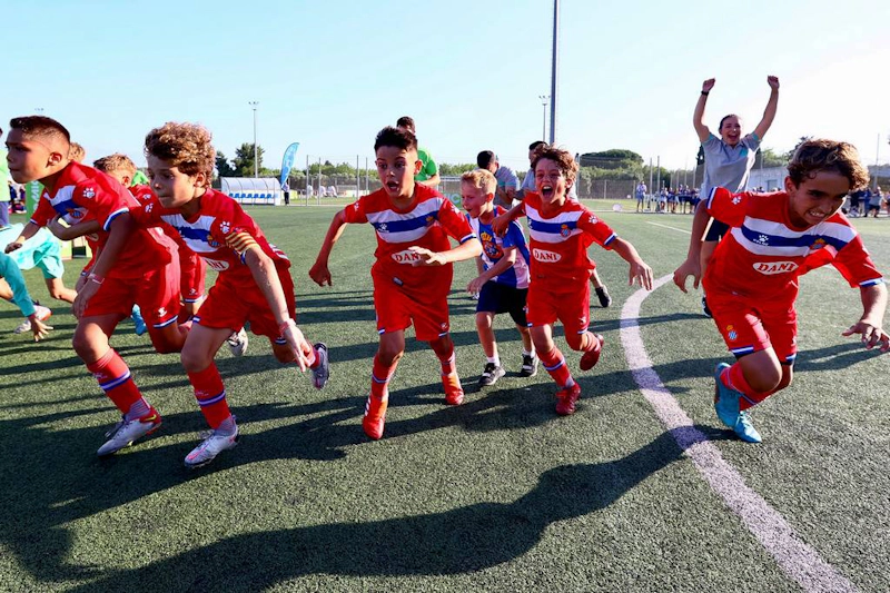 Jovens jogadores de futebol animados em uniformes vermelhos e azuis comemorando no torneio MICFootball 7