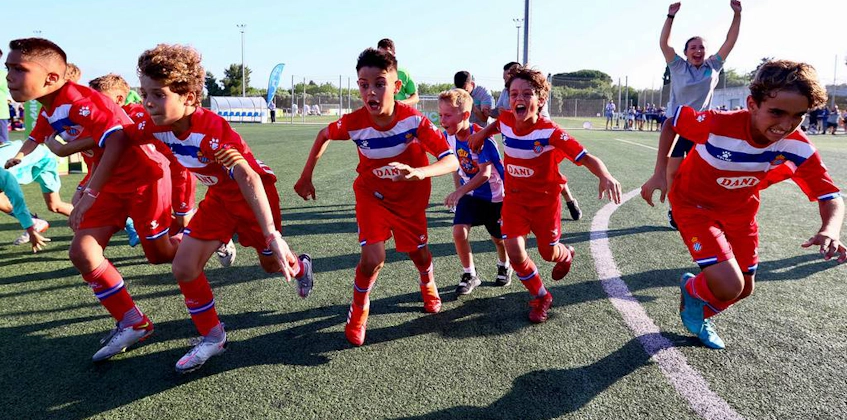 Excited young soccer players in red and blue kits celebrate at the MICFootball 7 tournament
