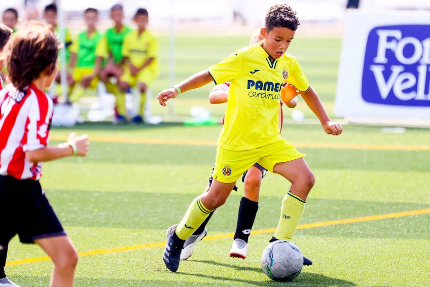 Młody piłkarz w żółtej koszulce kontroluje piłkę, z kolegami z drużyny w tle