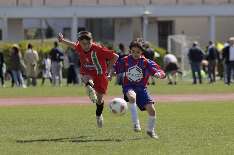 Два юных игрока в футболе в красной и сине-красной форме борются за мяч