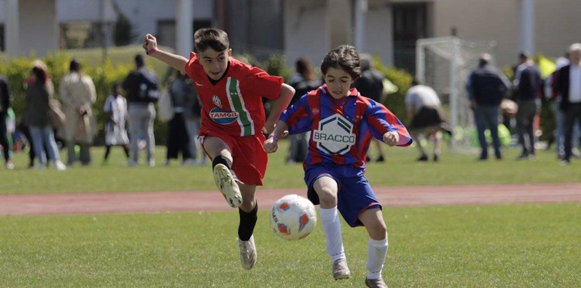 Two young soccer players in red and blue-red uniforms competing for the ball
