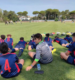 Equipo de fútbol juvenil en uniformes azules y rojos mirando un partido