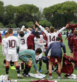 Jóvenes futbolistas celebran una victoria en un torneo, con entrenadores y jugadores al fondo