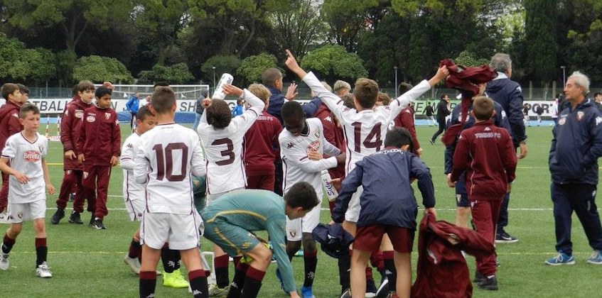 Giovani calciatori festeggiano una vittoria al torneo, allenatori e giocatori sullo sfondo