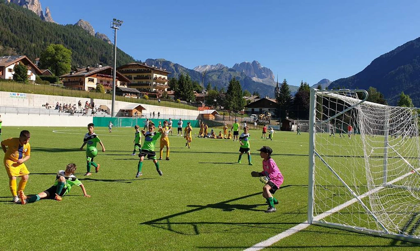 Crianças jogando futebol em Val di Fassa com montanhas ao fundo