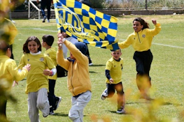 Χαρούμενα παιδιά με κίτρινα πουκάμισα τρέχουν σε γήπεδο ποδοσφαίρου με σημαίες