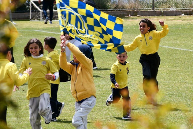 Fröhliche Kinder in gelben Hemden laufen mit Flaggen auf einem Fußballfeld