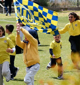 Niños alegres con camisetas amarillas corriendo en un campo de fútbol con banderas