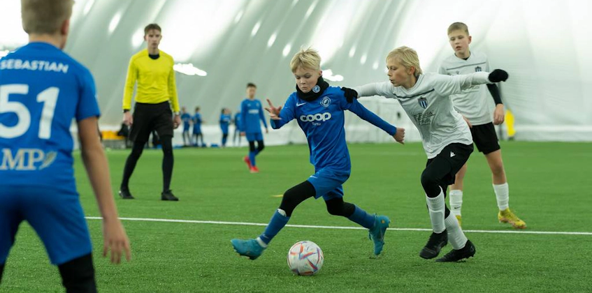 Dzieci w strojach sportowych grają w piłkę nożną na turnieju iSport February Cup