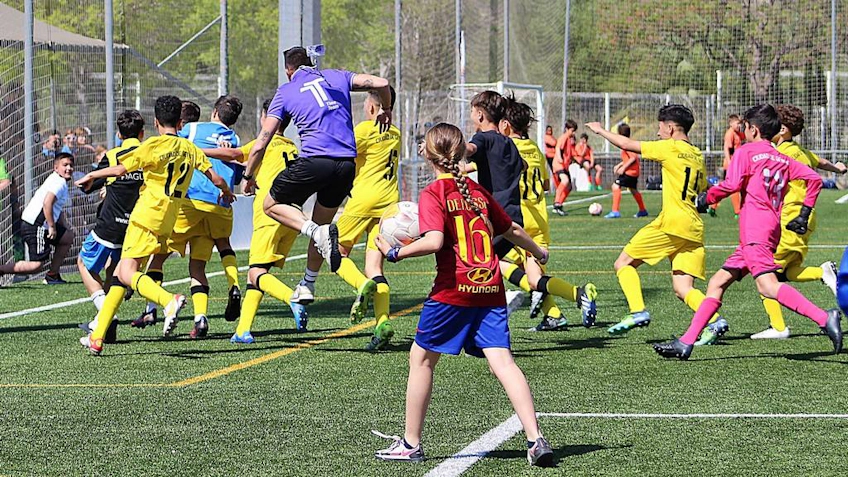 Football players in yellow kits playing on the field, one player in red kit observing