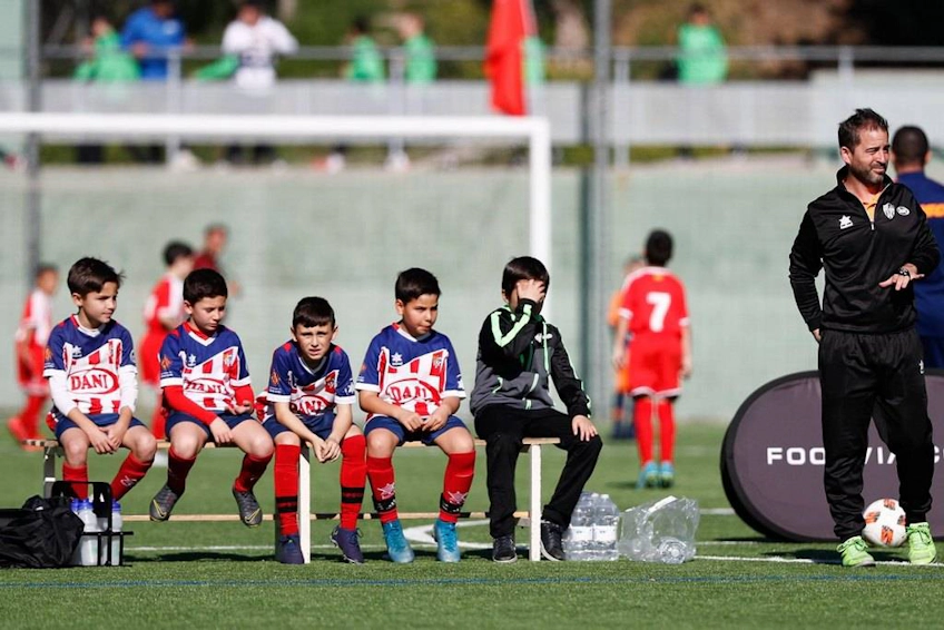 Young footballers and coach sitting on the bench at the side of the pitch during the FIT 24 Promises Edition tournament
