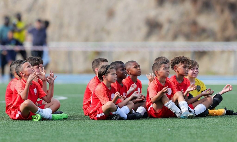 Children's football team in red jerseys sitting on the field at the FIT 24 Summer Edition tournament