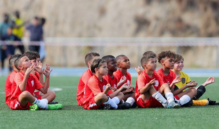 FIT 24 समर एडिशन टूर्नामेंट में मैदान पर बैठी लाल जर्सी में बच्चों की फुटबॉल टीम