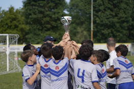 फुटबॉल मैदान पर युवा फुटबॉल खिलाड़ी ट्रॉफी उठाते हुए, टीम की जीत का जश्न