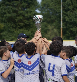 Nuoret jalkapalloilijat nostavat pokaalia jalkapallokentällä, joukkueen voitonjuhla