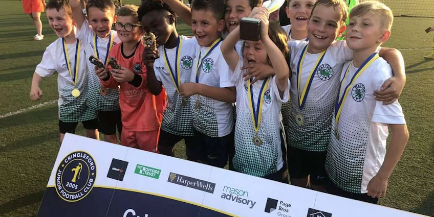 Young soccer team celebrates at Cringleford Cup with trophy.