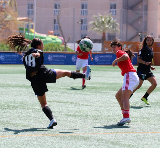 Jugadoras de fútbol en acción, una pateando el balón en el aire durante un partido