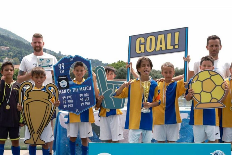 Equipo de fútbol juvenil con entrenadores sosteniendo un trofeo y accesorios de fútbol en el torneo Trofeo Mar Tirreno