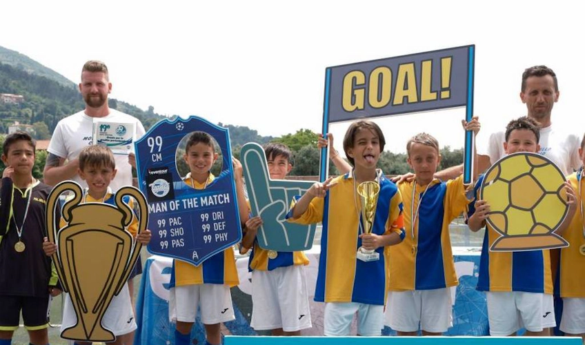 Youth football team with coaches holding a trophy and football props at the Trofeo Mar Tirreno tournament