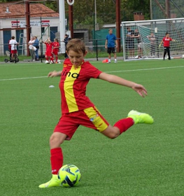 Chłopiec w czerwonym stroju kopiący piłkę na turnieju Ixina Cup