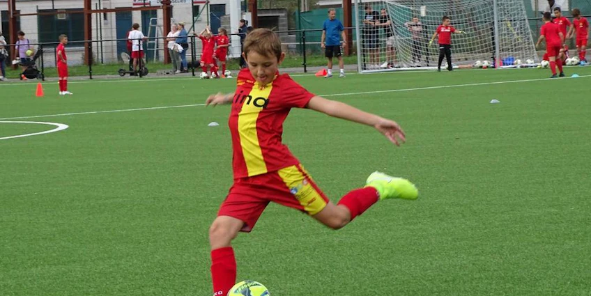 Băiat în echipament roșu șutând o minge de fotbal la turneul Ixina Cup