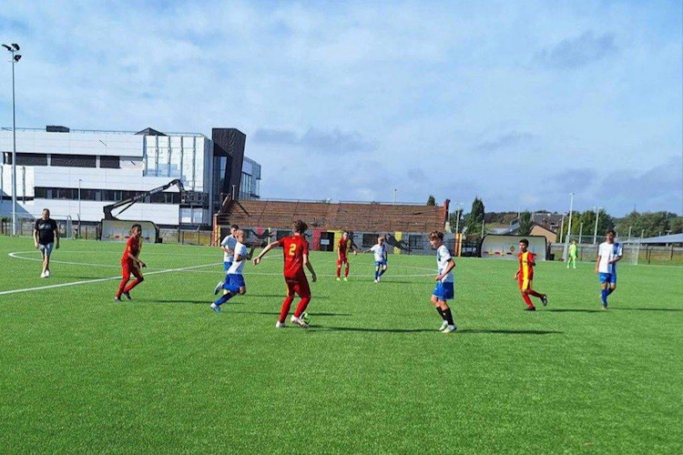 Meci de fotbal pentru tineret pe teren verde cu echipe în roșu și albastru