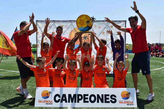 청소년 축구팀이 'Campeones' 배너와 함께 발렌시아 비치 토너먼트에서 승리를 축하합니다.