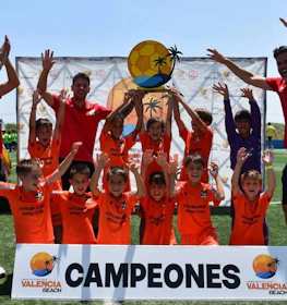Echipa de fotbal tineret sărbătorește victoria la turneul Valencia Beach cu antrenori și bannerul 'Campeones'.