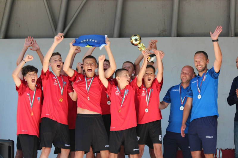 Tineri fotbaliști în tricouri roșii sărbătorind o victorie în turneu