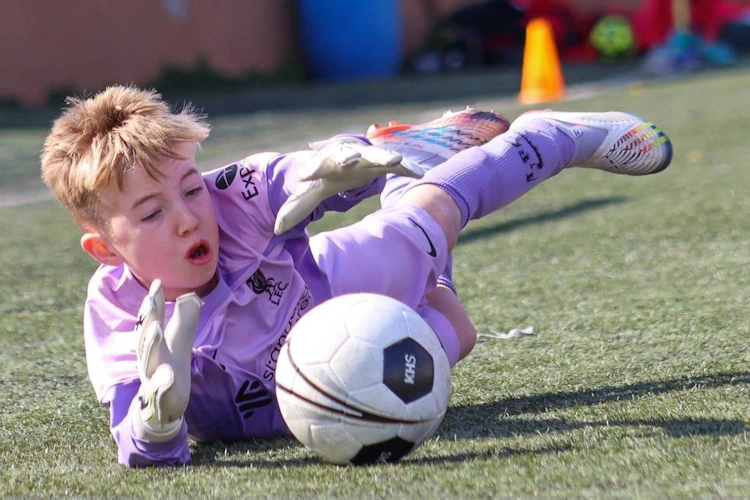 Mor libaslı gənc qapıçı futbol oyununda topu dəf edir