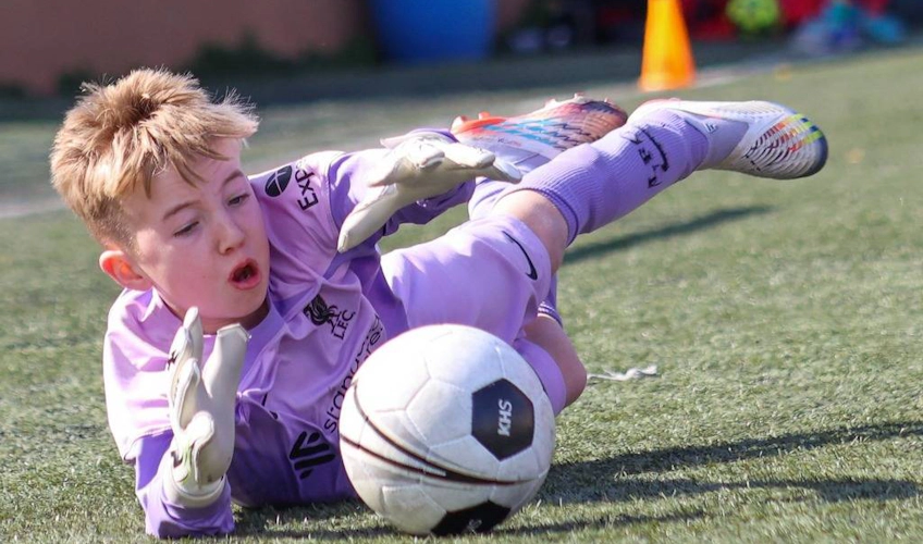 サッカーの試合でセーブをする紫色のユニフォームの若いゴールキーパー