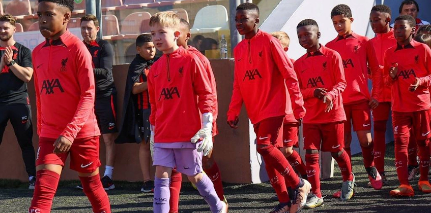U10 KHS कप में लाल किट में युवा फुटबॉल टीम मैदान में चलती हुई