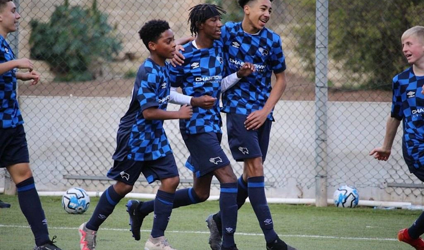 Νεαροί U13 με μπλε και μαύρες ρίγες πανηγυρίζουν ένα γκολ στο γήπεδο