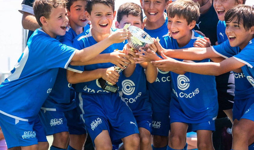 Équipe de jeunes footballeurs en tenue bleue tenant joyeusement un trophée au tournoi
