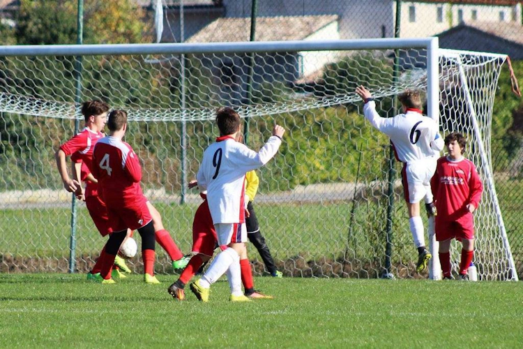 Jugendliche Fußballspieler im Einsatz, einer springt, um den Ball nahe am Tor zu köpfen