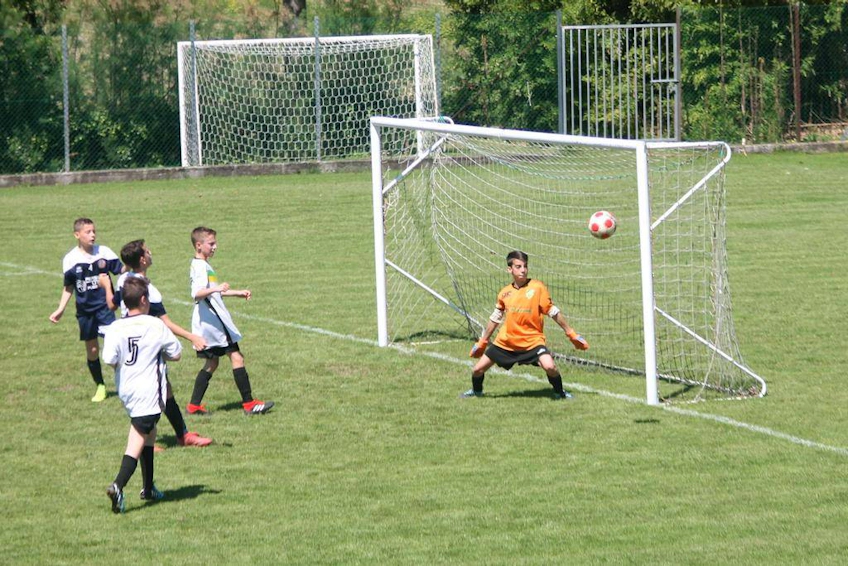 Youth football match with a goalie in orange ready to save a goal as the ball approaches the net.