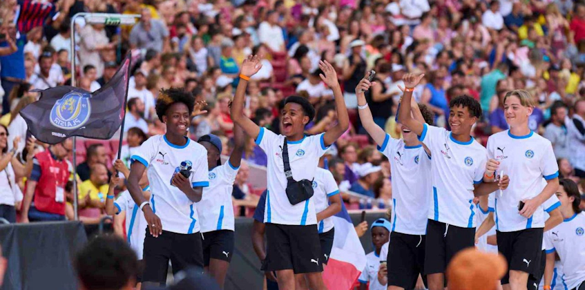 Χαρούμενοι νέοι ποδοσφαιριστές πανηγυρίζουν στο στάδιο με σημαία MADCUP