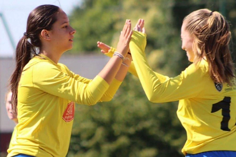 Dos chicas con camisetas amarillas de fútbol celebran con un choque de manos en un torneo