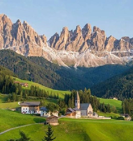 قرية في جبال الدولوميت مع كنيسة في بطولة Grand Prix Dolomites Summer Trophy محاطة بالجبال والغابات.