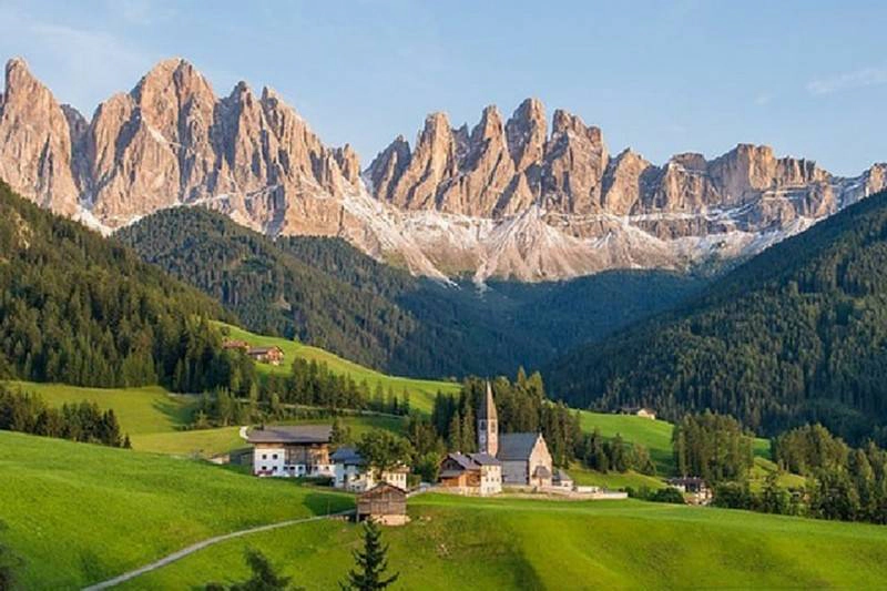 Dorf in den Dolomiten mit einer Kirche beim Grand Prix Dolomites Summer Trophy Turnier, umgeben von Bergen und Wäldern.