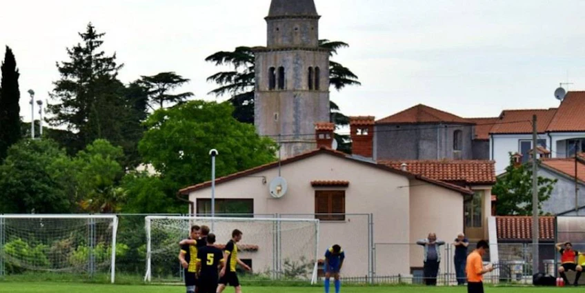 Fodboldkamp ved Grand Prix Poreč Summer Trophy med en kirke og træer i baggrunden.