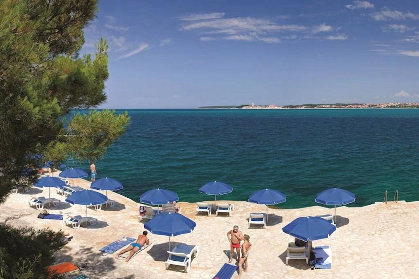 Beautiful beach with blue umbrellas and sun loungers on the Adriatic Sea coast overlooking Poreč, Croatia.